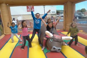 Des enfants qui lèvent les bras sur un taureau gonflable situé dans un château gonflable.