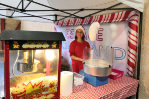 espace gourmand avec une machine a pop corn, une barbe a papa et une jeune fille qui tiens le stand