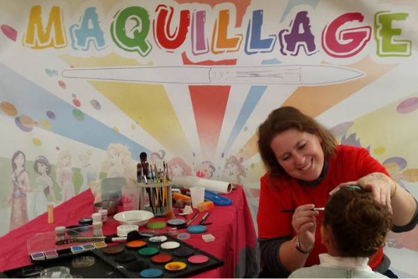 un stand maquillage. Une femme qui sourit en maquillant une petite fille